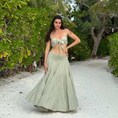 Woman in a green dress standing on a sandy path with greenery around