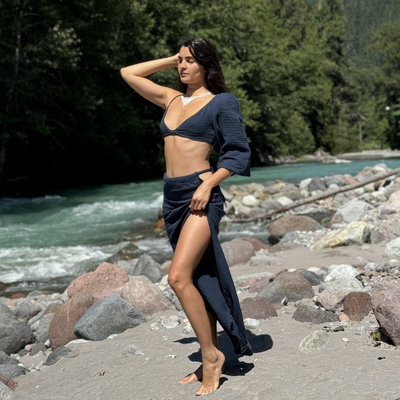 Woman in a blue outfit standing by a river with mountains in the background